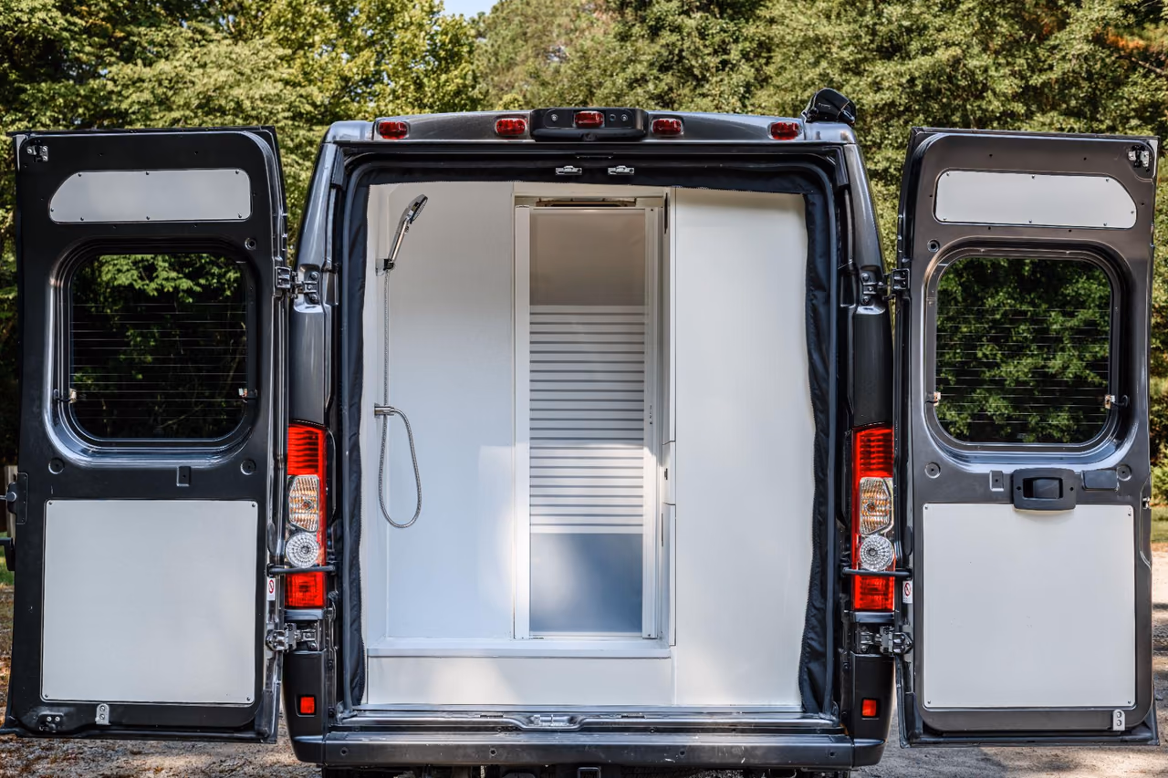 Custom camper van shower viewed through the open rear doors with a privacy door closed.