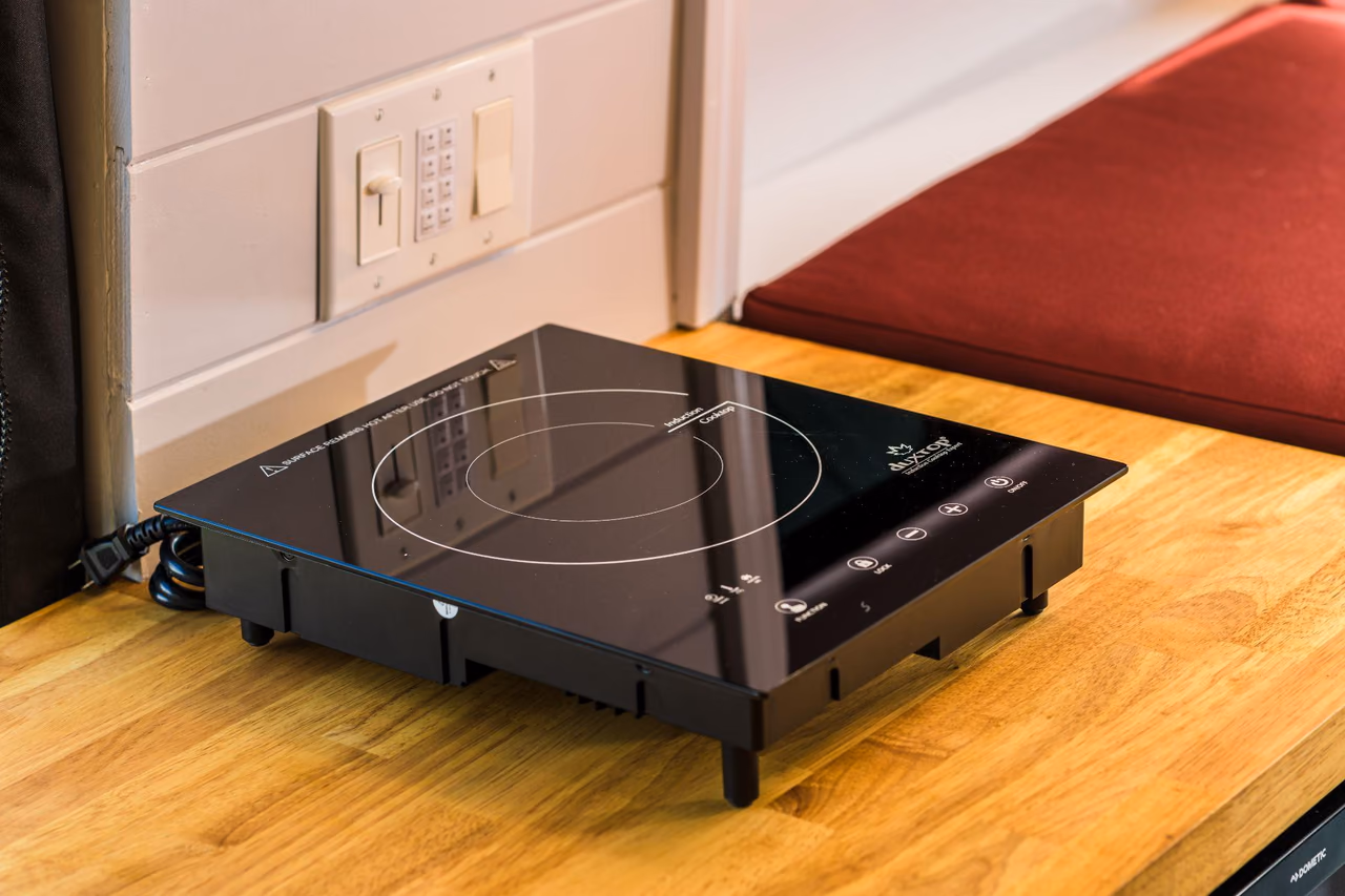 Portable induction cooktop on a natural wood countertop inside a custom camper van kitchen.