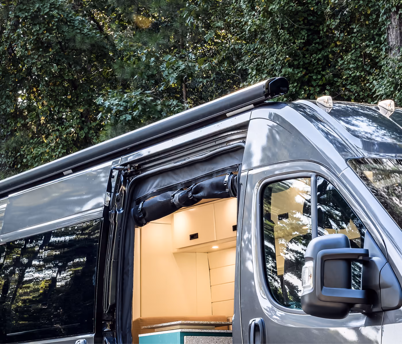 Retractable awning mounted above the sliding door of a camper van with a rolled-up bug screen across the doorway.