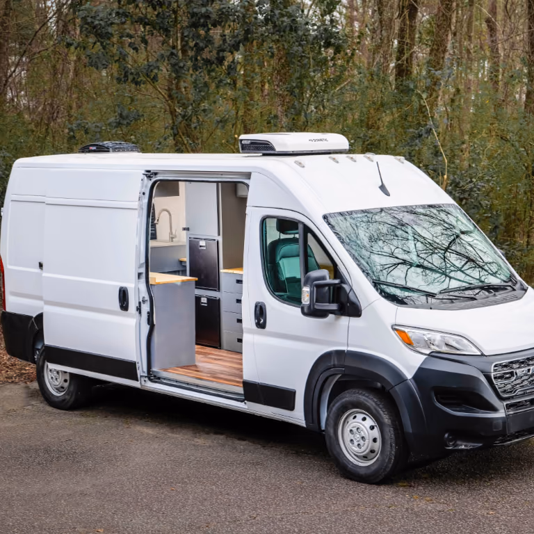 White commercial van with the sliding door open, showing wood counters, gray cabinetry, a sink, and storage inside.