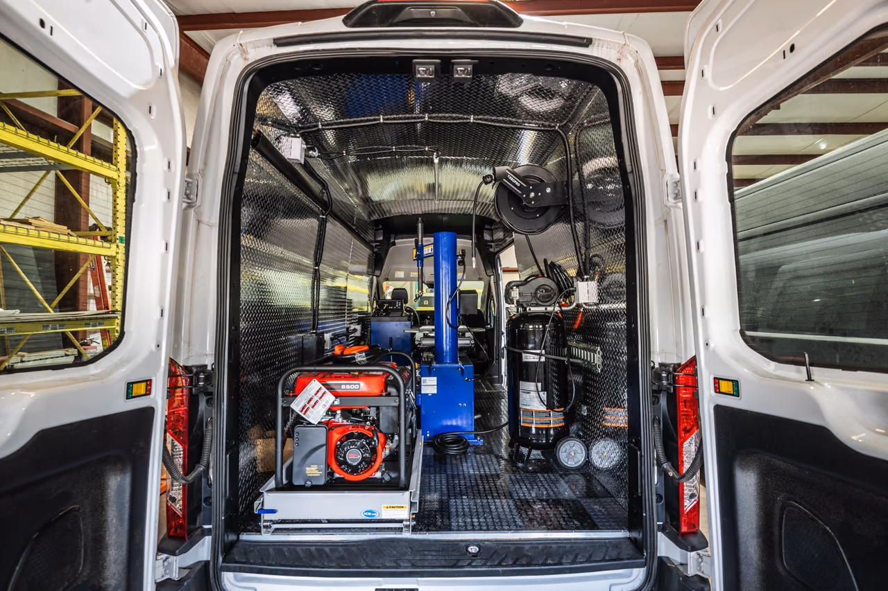 Rear view of a custom mobile tire service van with tire equipment, an air compressor, and a generator inside a diamond-plate interior.