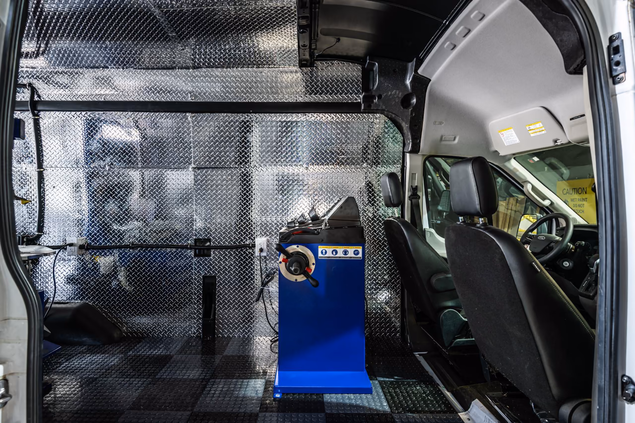 Tire balancing machine behind the cab of a mobile tire service van with diamond-plate walls and patterned flooring.