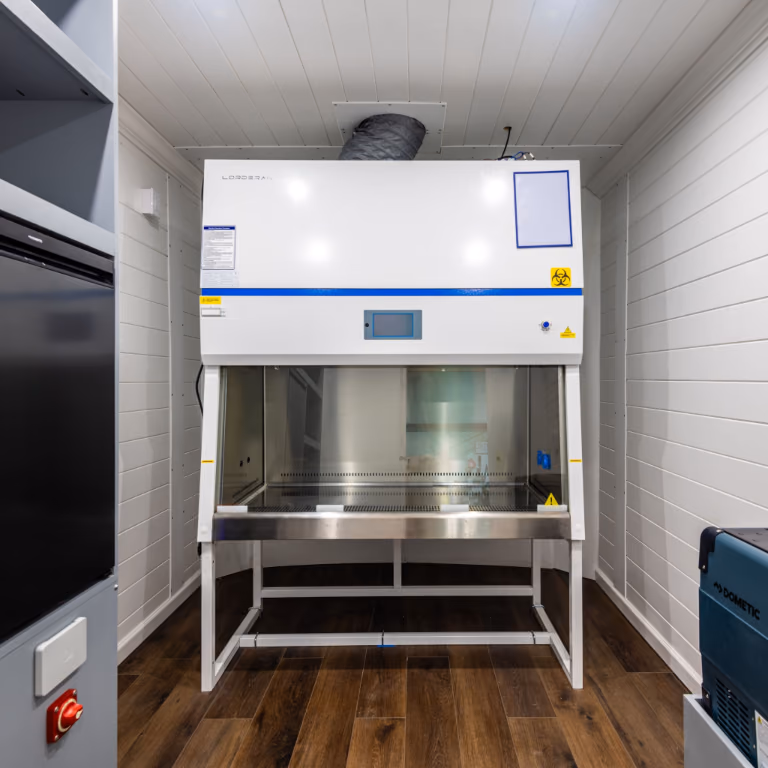 Large enclosed workstation fitted inside the van with overhead ducting, white wall panels, and wood-look flooring.