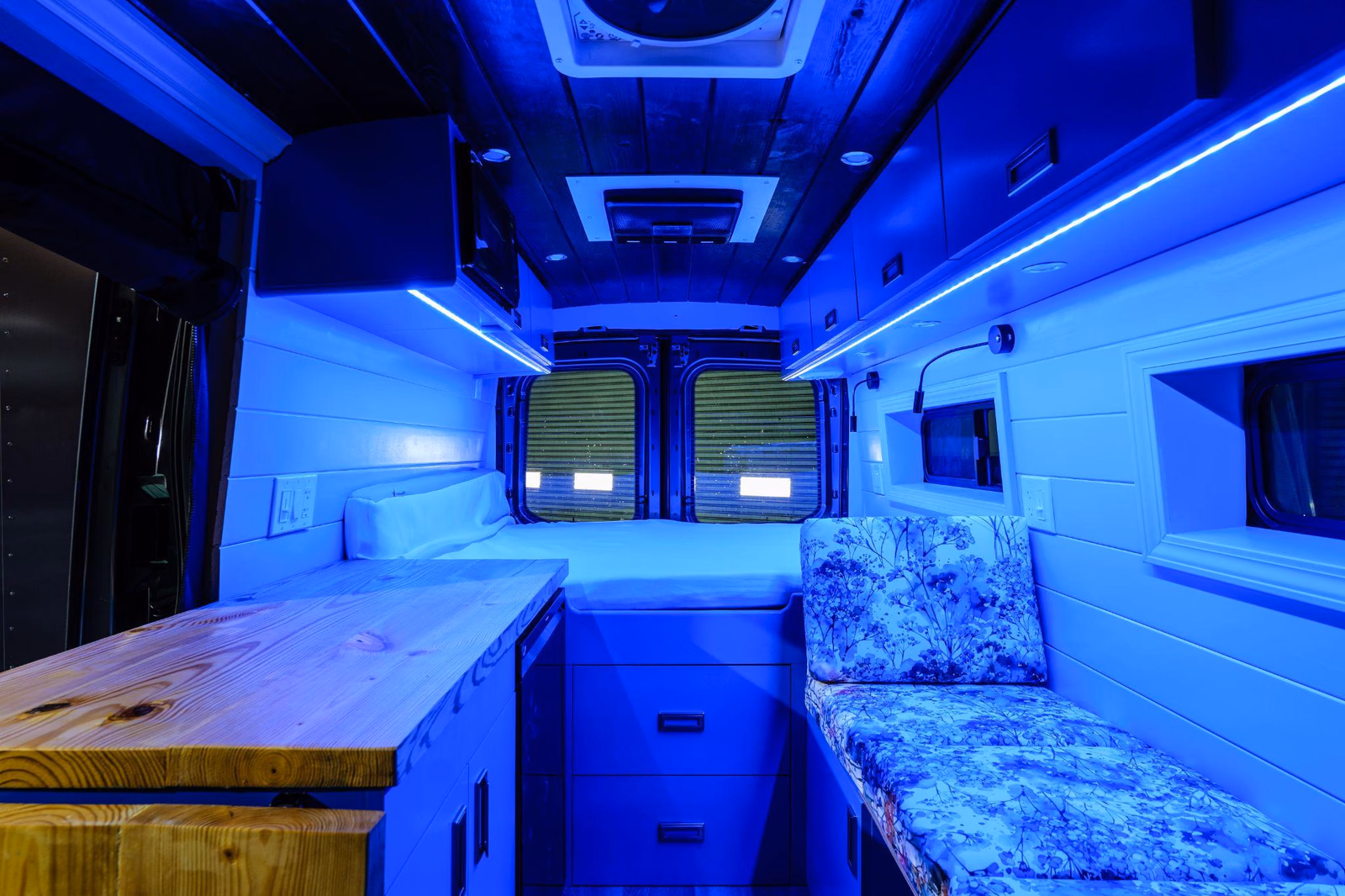 Blue LED strip lighting illuminating the cabinetry and seating inside a custom camper van.
