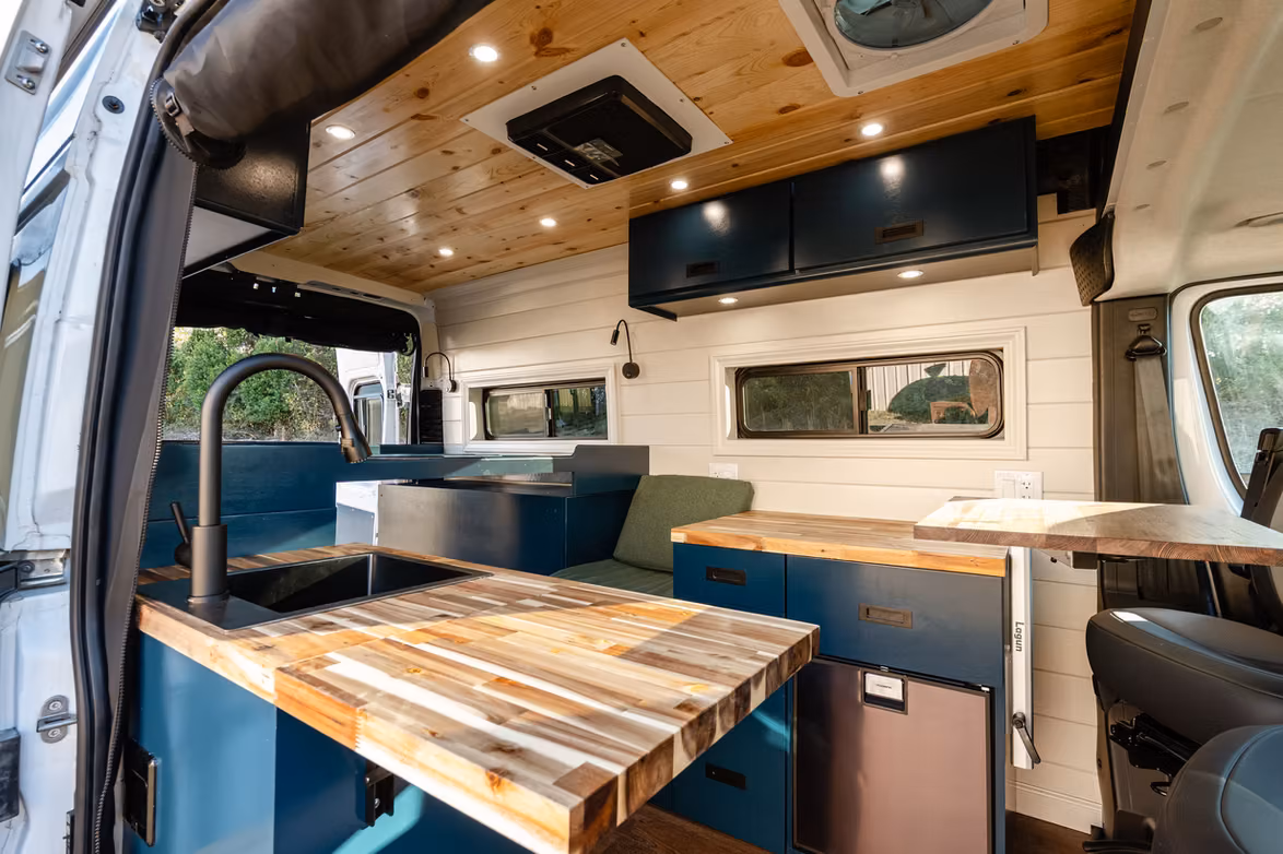 Custom campervan interior with painted cabinets, a wood dining table, and kitchen storage
